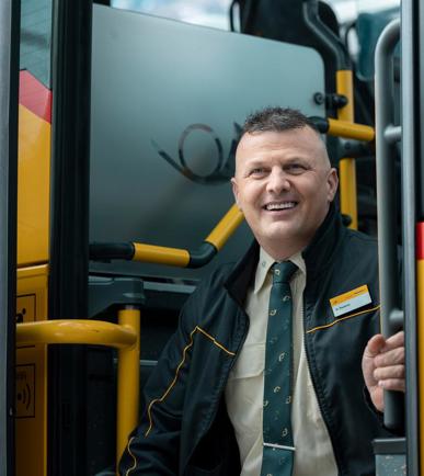 Ein Postauto-Mitarbeiter, der bei der Eingangstreppe eines Postautos sitzt und lacht